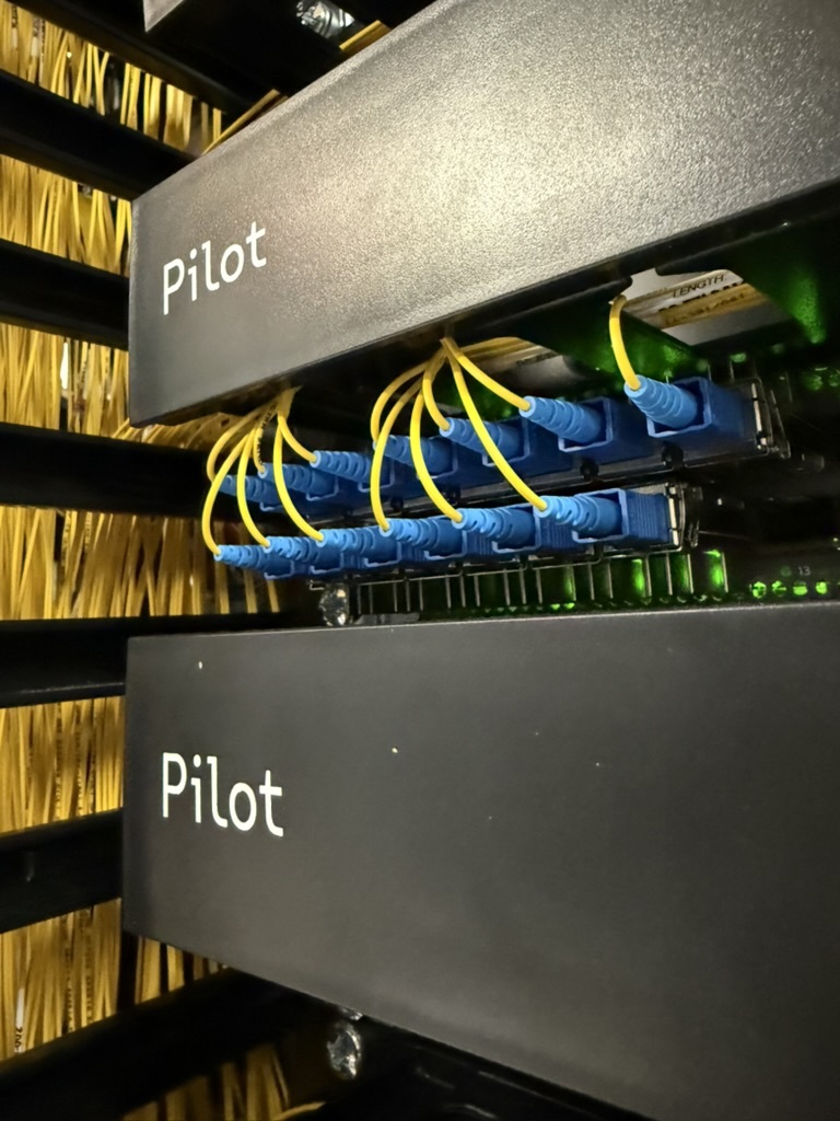 Pilot-branded fiber patch panels in a data center rack, with blue connectors and yellow fiber jumpers